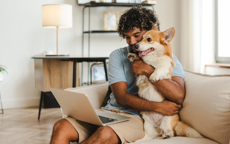 man hugs dog while sitting on a couch looking at his laptop