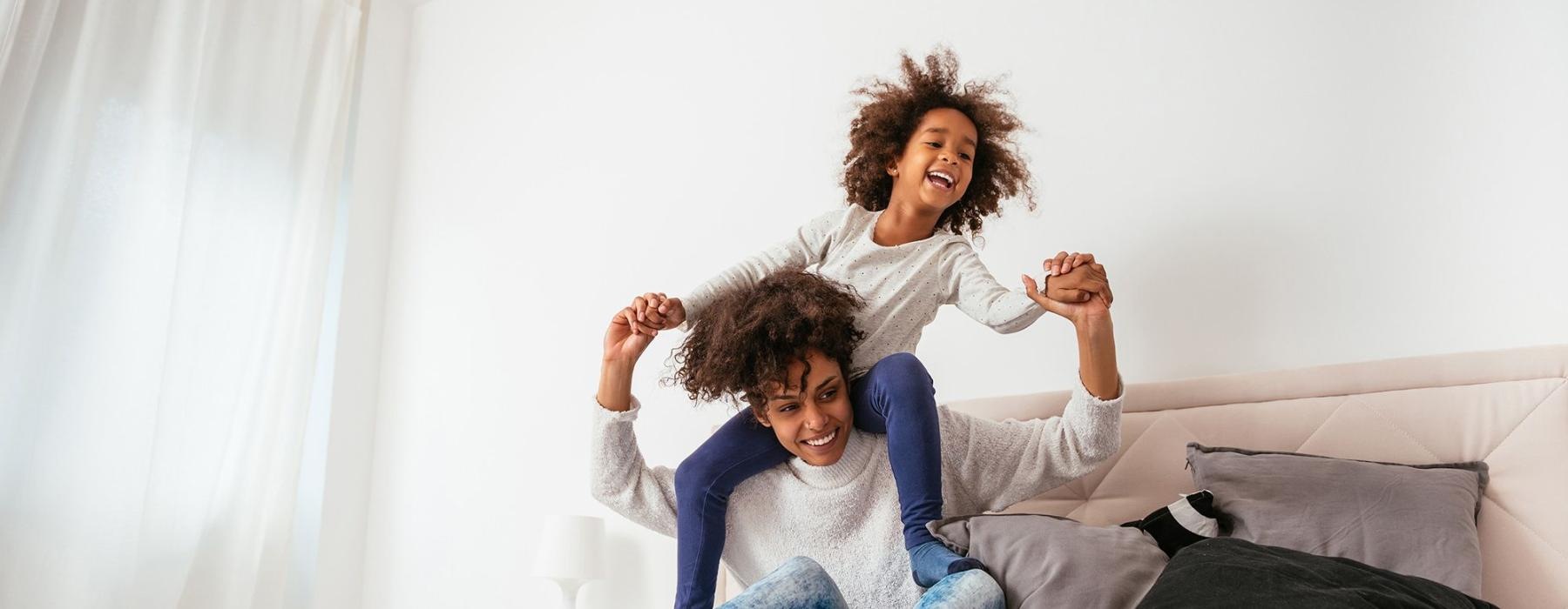mother and daughter happily play on a large bed